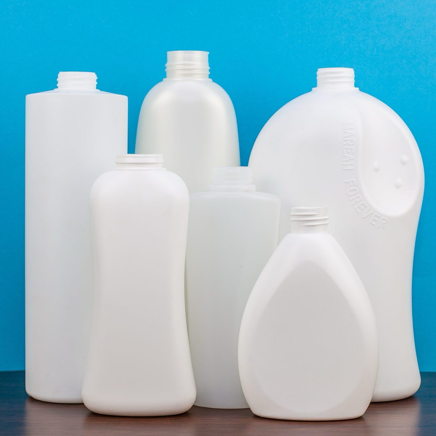 Six white HDPE blow-moulded bottles on a blue backdrop, from CJ Polymers' product photography