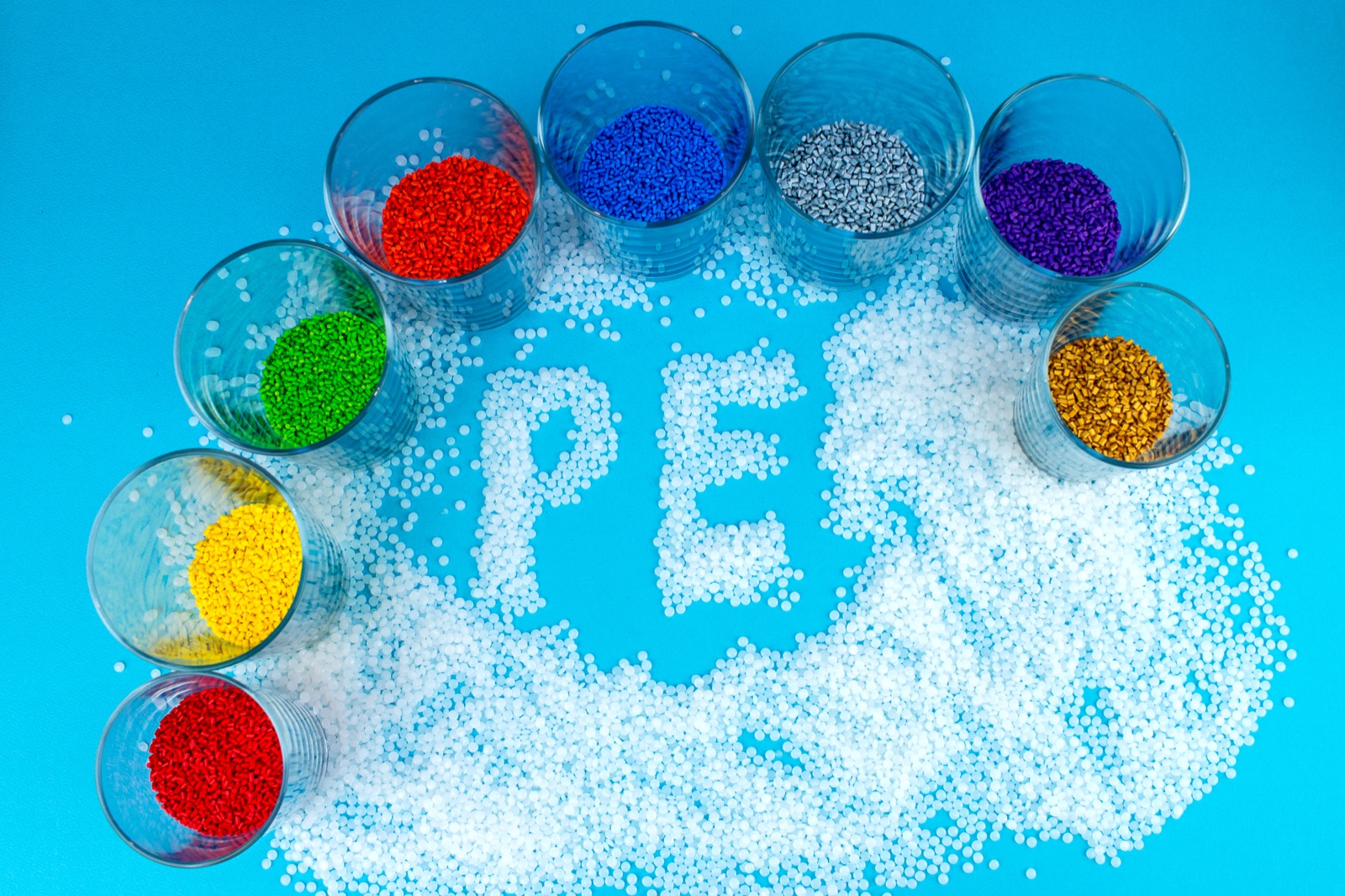 Polyethylene pellets with cups of coloured masterbatch on a blue backdrop, from CJ Polymers' product photography