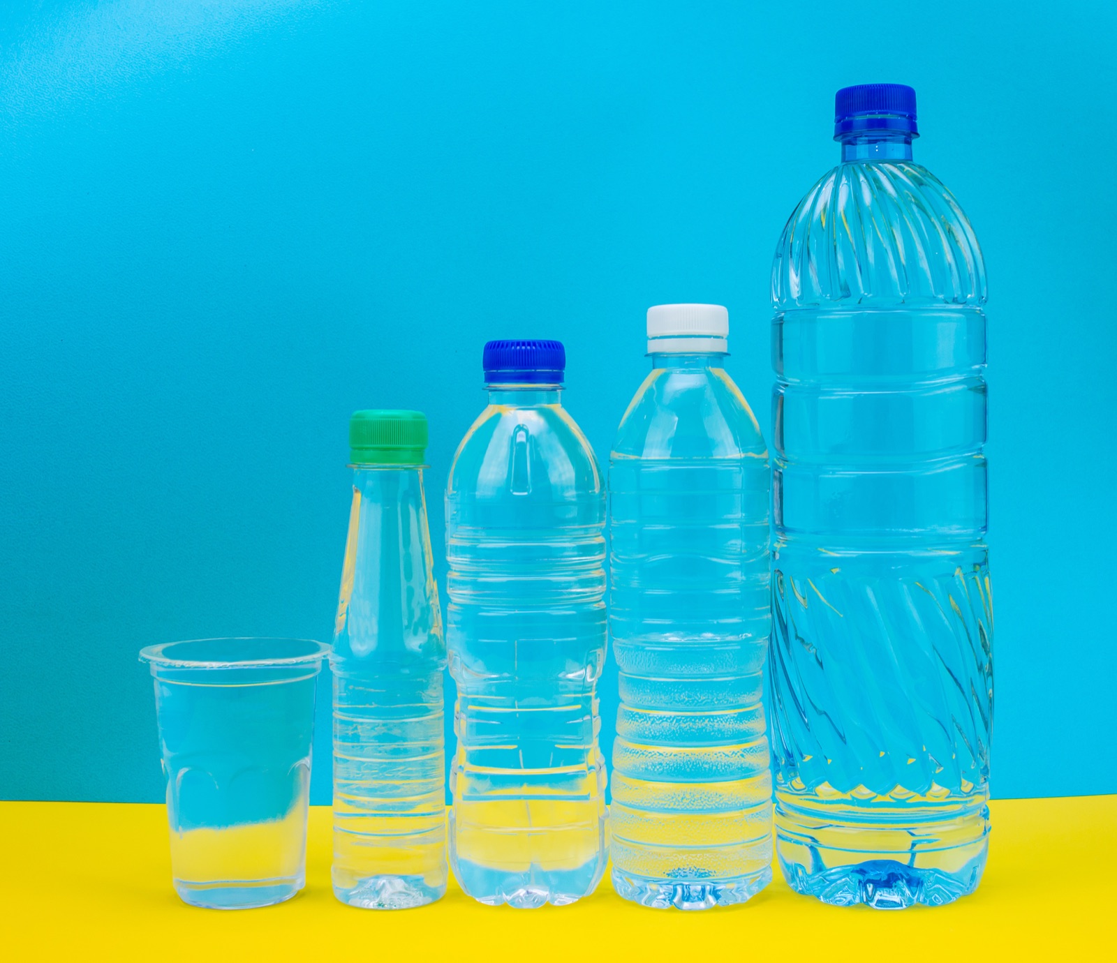 Five clear PET bottles of increasing size on a cyan and yellow backdrop, from CJ Polymers' product photography