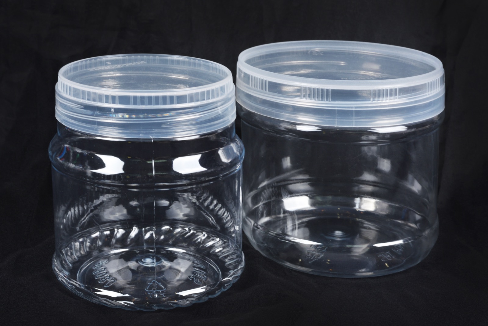 Two clear PET jars with lids on a black backdrop, from CJ Polymers' product photography