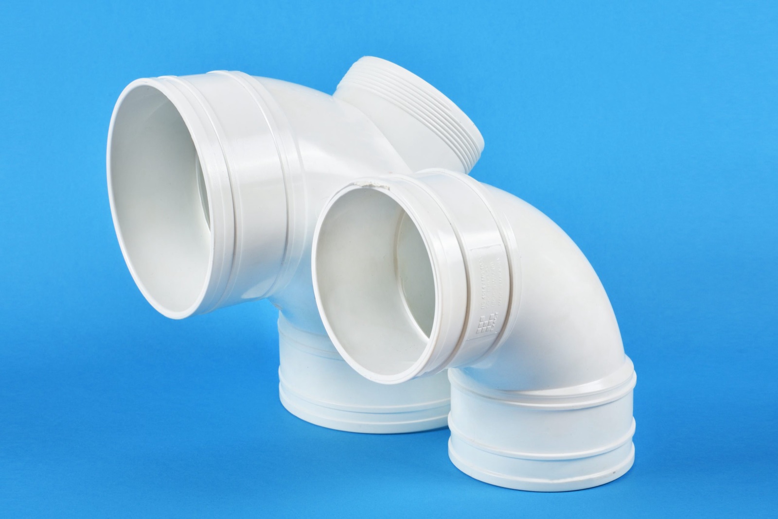 White PVC pipe fittings on a blue backdrop, from CJ Polymers' product photography